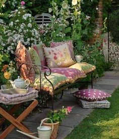 an outdoor seating area with flowers and potted plants on the ground, in front of a garden