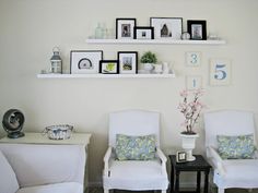 two white chairs sitting next to each other in front of a wall with pictures on it