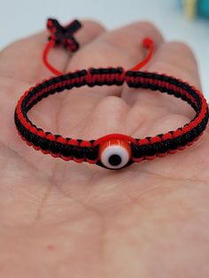 a hand holding a red and black bracelet with an evil eye bead on it