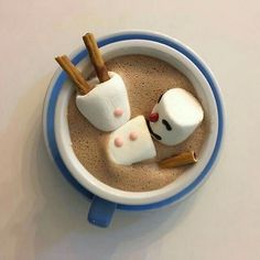 two marshmallows in a cup with cinnamon sticks sticking out of them