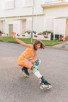 a woman riding a skateboard down a street next to a white house and green grass