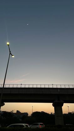 the sun is setting on an overpass and cars are parked under it