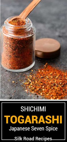 a jar filled with red spices next to a wooden spoon on top of a table