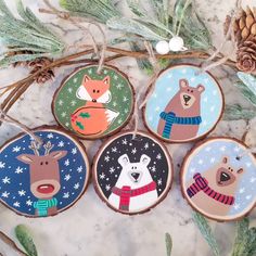 four wooden ornaments with animals on them and pine cones in the background, all decorated to look like christmas trees