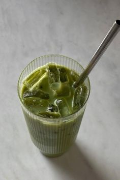 a glass filled with green liquid on top of a white table next to a spoon