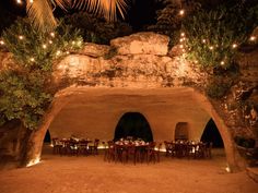 an outdoor dining area is lit up at night with lights strung from the ceiling and tables set for dinner