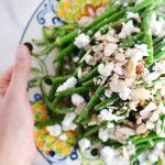 a plate with green beans, feta cheese and someone's hand on it