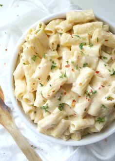 a white bowl filled with macaroni and cheese on top of a table next to a wooden spoon