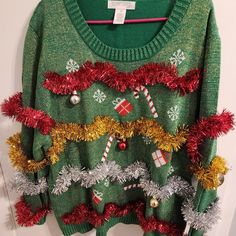 a green sweater with christmas decorations on it and red, white and yellow tinsel