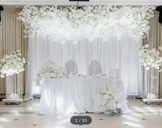 a table with white flowers on it in front of a curtained wall and chandelier