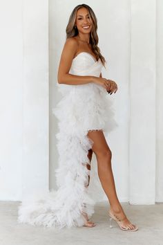 a woman posing in a white dress with feathers on the bottom and side, wearing high heeled sandals