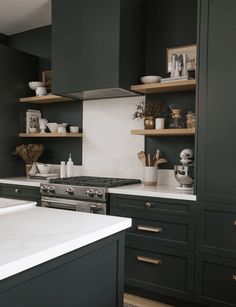 a kitchen with dark green cabinets and white counter tops, gold trim on the shelves