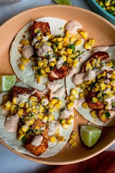 three tacos on a plate with lime wedges and salsa in the bowl next to it