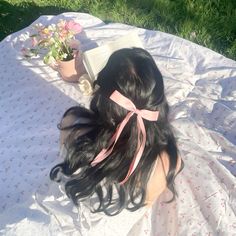 a woman laying on top of a white blanket next to a potted plant and book