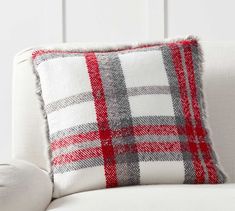 a white couch with a red and gray plaid pillow on it's backrest