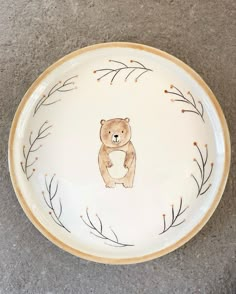 a white plate with a brown bear painted on the side and branches in the middle