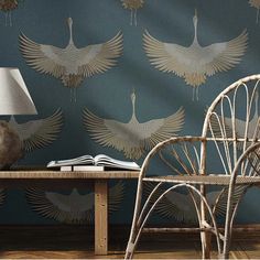 a chair and table with a lamp on it in front of a peacock wallpaper