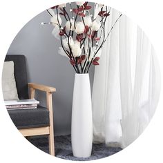 a white vase with flowers in it sitting on a table next to a gray chair