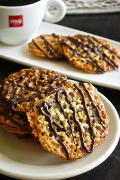 two cookies with chocolate drizzled on them next to a cup of coffee