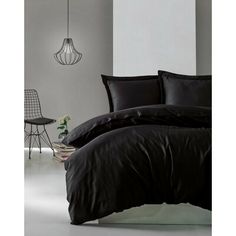 a bed with black sheets and pillows in a white room next to a chair, table and lamp