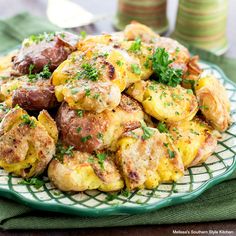 a green plate topped with potatoes covered in cheese and parsley on top of a table