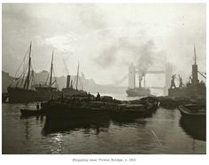 an old black and white photo of several boats in the water with a bridge in the background