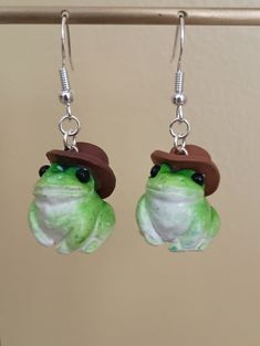 the frog is wearing a brown hat and green earring with beads on it's ears