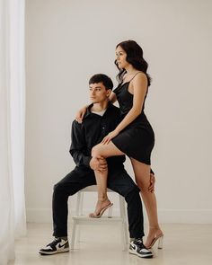 a man sitting on a chair next to a woman in a black dress and high heels