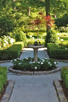 a small fountain in the middle of a garden with white flowers and greenery around it