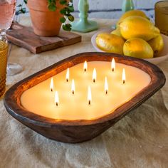 a lit candle in a wooden bowl on a table with lemons and limes