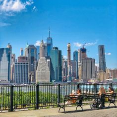 two people sitting on benches in front of a city skyline with tall buildings and skyscrapers