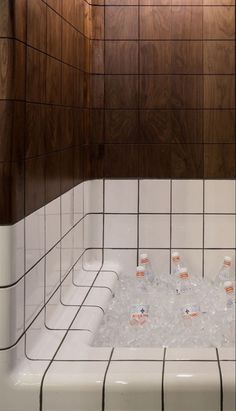 a bathtub filled with lots of ice and water next to wooden paneled walls