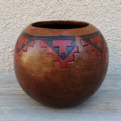 a brown vase with red and black designs on the outside, sitting on a wooden table