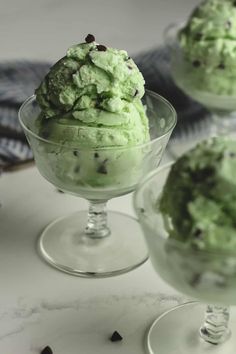 two glasses filled with green ice cream on top of a white table next to chocolate chips