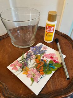 some flowers are sitting on top of a table next to a glass bowl and brush