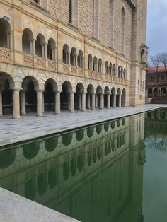 an empty pool in front of a large building with arches and columns on the sides