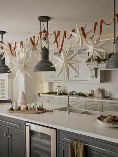 a kitchen decorated for christmas with lights and paper snowflakes hanging from the ceiling