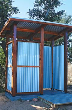 a small blue metal structure sitting in the middle of a dirt field next to trees