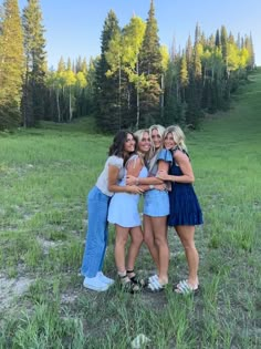 four women standing together in a field with trees in the background