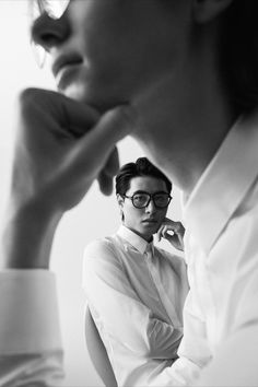 a woman wearing glasses sitting next to a man in a white shirt and tie with his hand on his chin