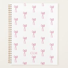 a spiral notebook with pink bows and the word cm printed on it, in front of a white background