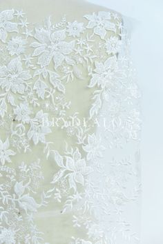 the back of a wedding dress with white lace on it and flowers in the center