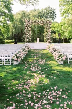 an outdoor ceremony set up with white chairs and pink flowers on the grass in front of it