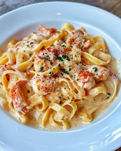 a white plate topped with pasta covered in sauce and shrimp next to a slice of bread