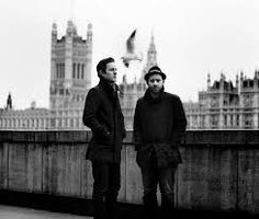 two men standing next to each other in front of a building with a bird flying over them