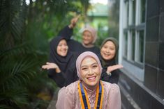 three women in hijabs are smiling and posing for the camera with their arms outstretched