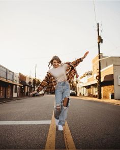 a woman is walking down the street with her arms spread out and she's wearing ripped jeans