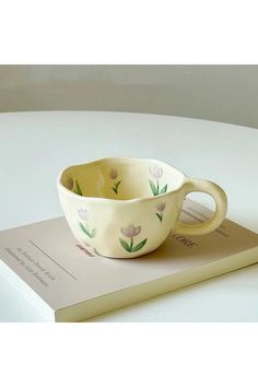 a white and yellow bowl sitting on top of a book with flowers painted on it