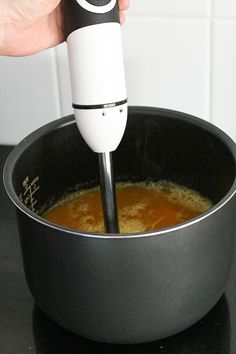 a hand is using a blender to mix food in a pot