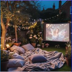 an outdoor movie is set up in the backyard with lights strung from trees and potted plants